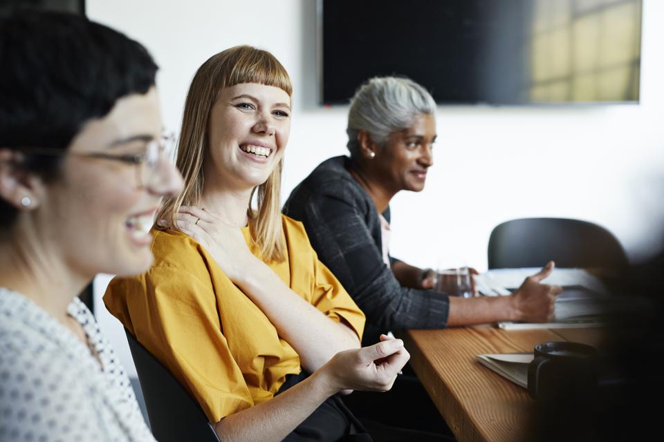 Three women of different ages and races sit in a board room.