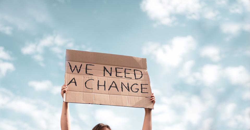 Woman holding a banner of 'We Need A Change'.