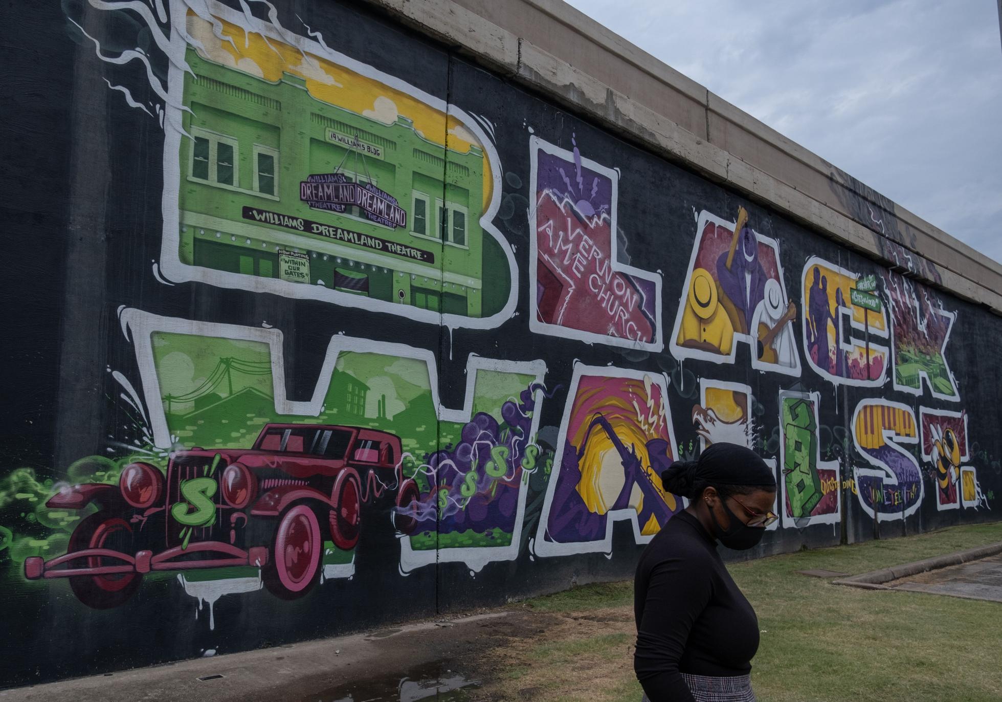 A woman walking in front of a mural for Black Wall Street