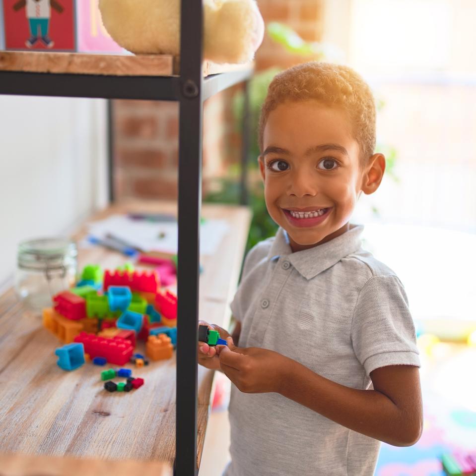 Beautiful african american toddler standing playing with small building blocks on shelving at kindergarten