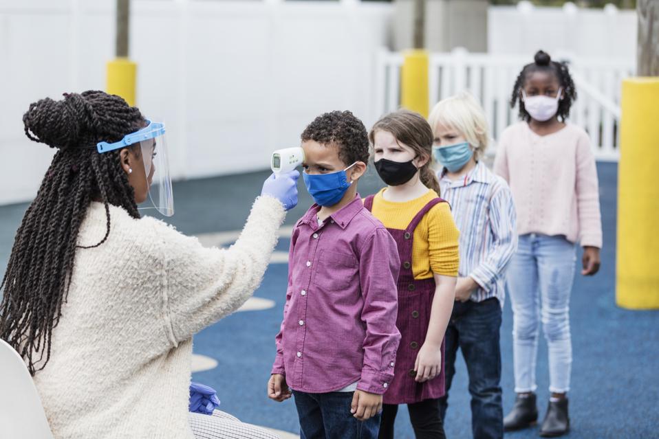Four children wait in line to have their temperatures checked with a forehead thermometer.
