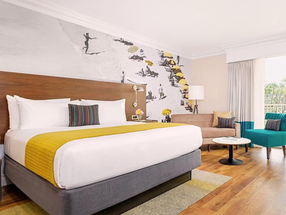 A hotel room with a bed, seating area and surf-themed mural