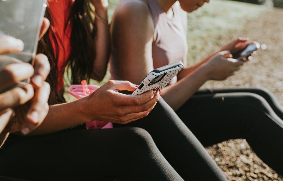 Trois femme tenant leurs téléphones portables à l'extérieur et regardant les écrans