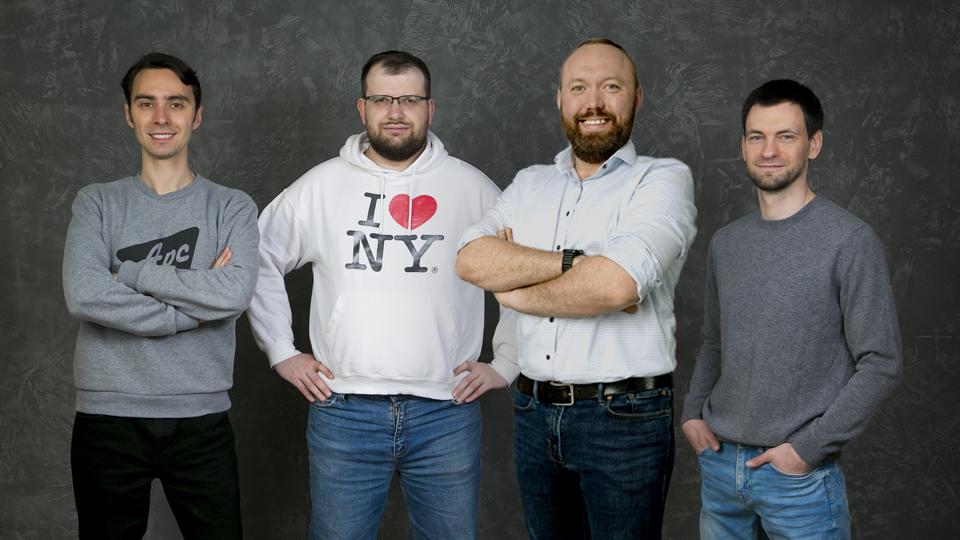 Four guys standing and smile with a grey background.