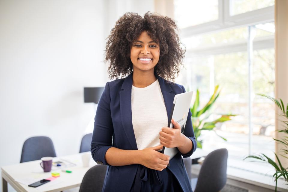 A young woman intern smiles holding a folder in an office.