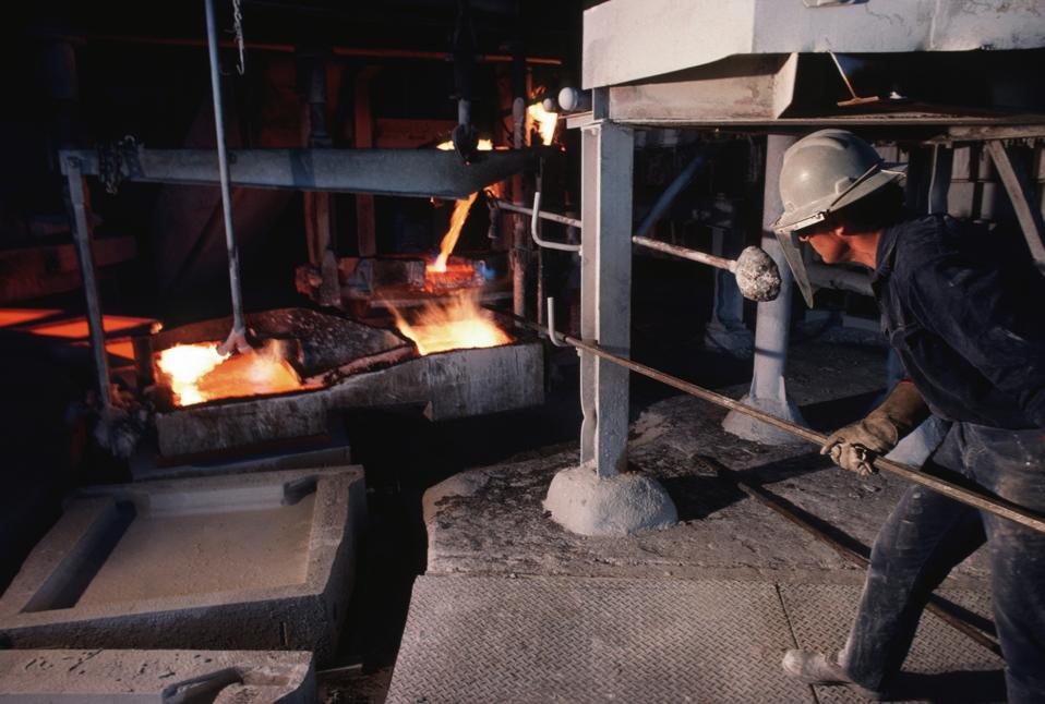 A foundry worker helps as molten iron is poured into moulds...