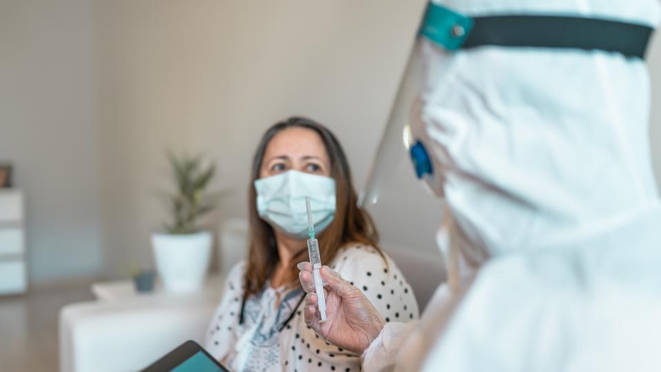 Female Doctor in protective gloves and workwear preparing Covid-19 Vaccine for patient