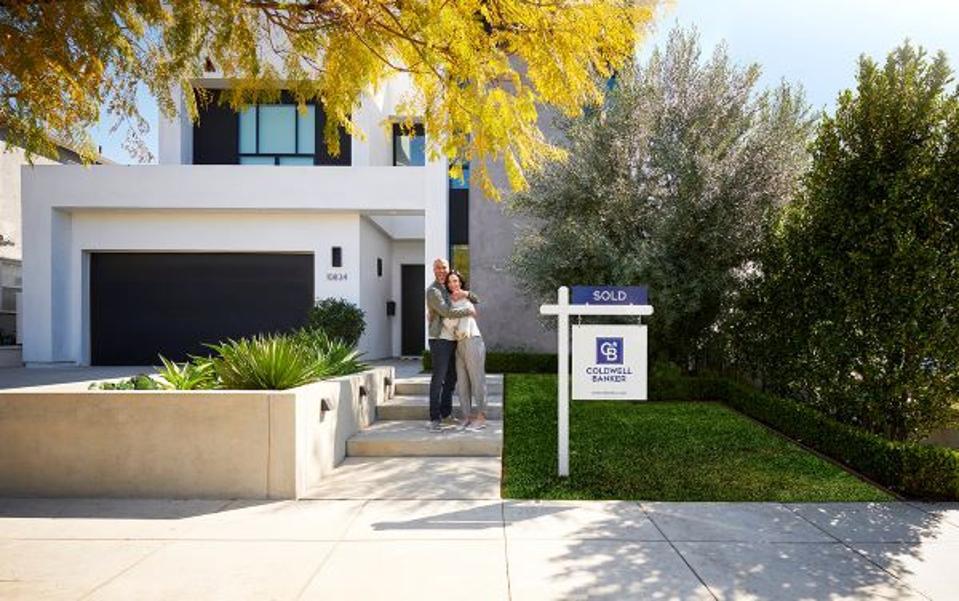 couple hugging in front of home with sold sign