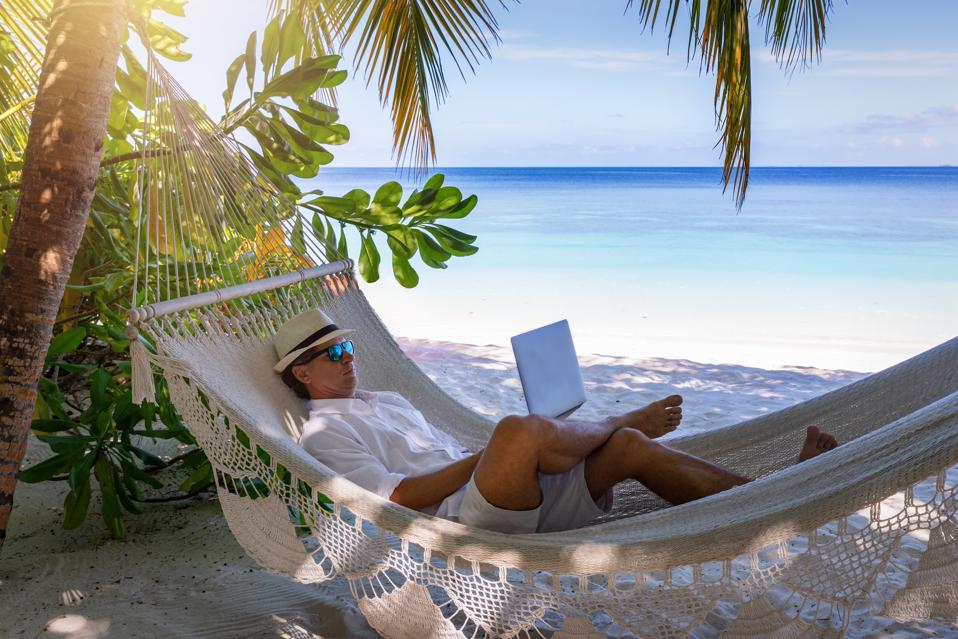 Man Using Laptop While Relaxing In Hammock At Beach Against Sky