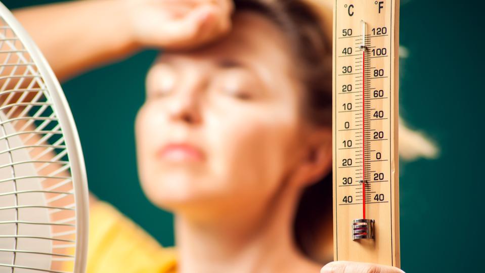 A portrait of woman in front of fan suffering from heat holding thermometer. Close up. Hot weather concept