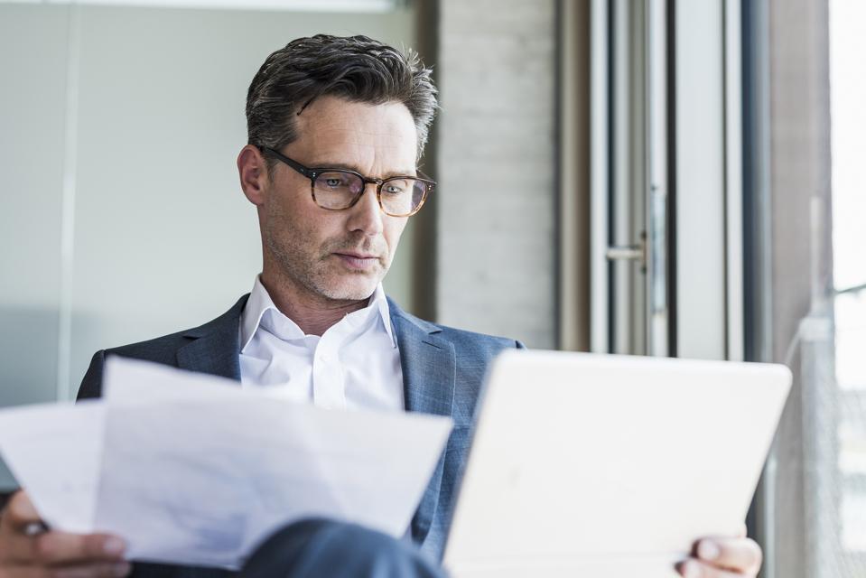 Portrait of serious businessman with documents looking at tablet