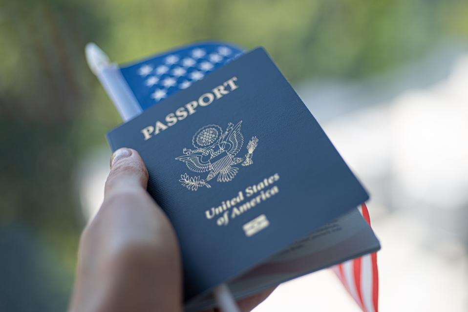 Passport of United states of America and flag of USA  in hand on green blurred background.