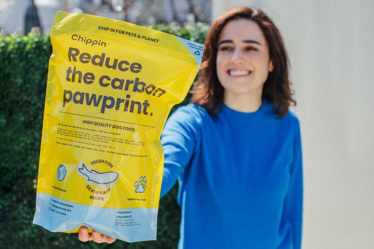Woman hold a bag of dog food with writing on it: ″Reduce the carbon pawprint.″