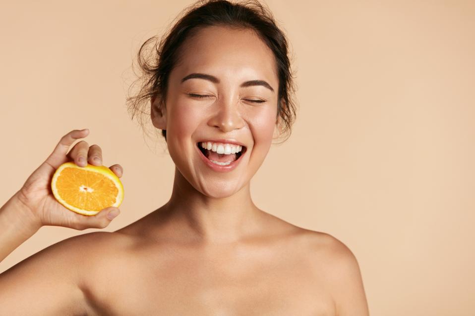 Smiling woman laughs while squeezing an orange. 