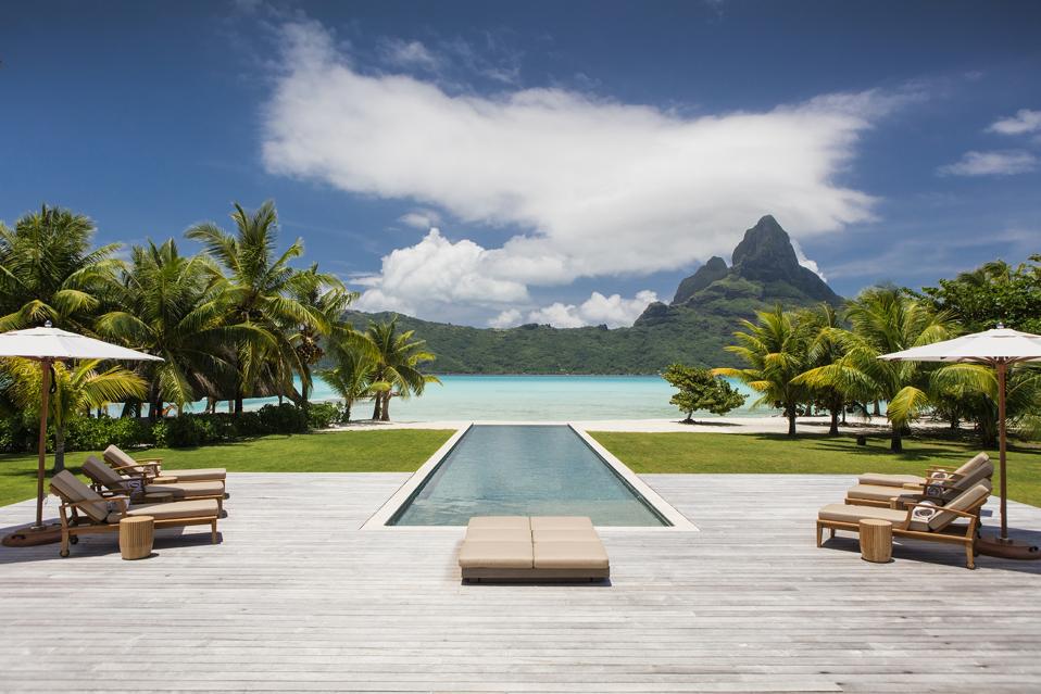 Terrasse de piscine en bois avec chaises face à l'île principale de Bora Bora et au mont Otemanu