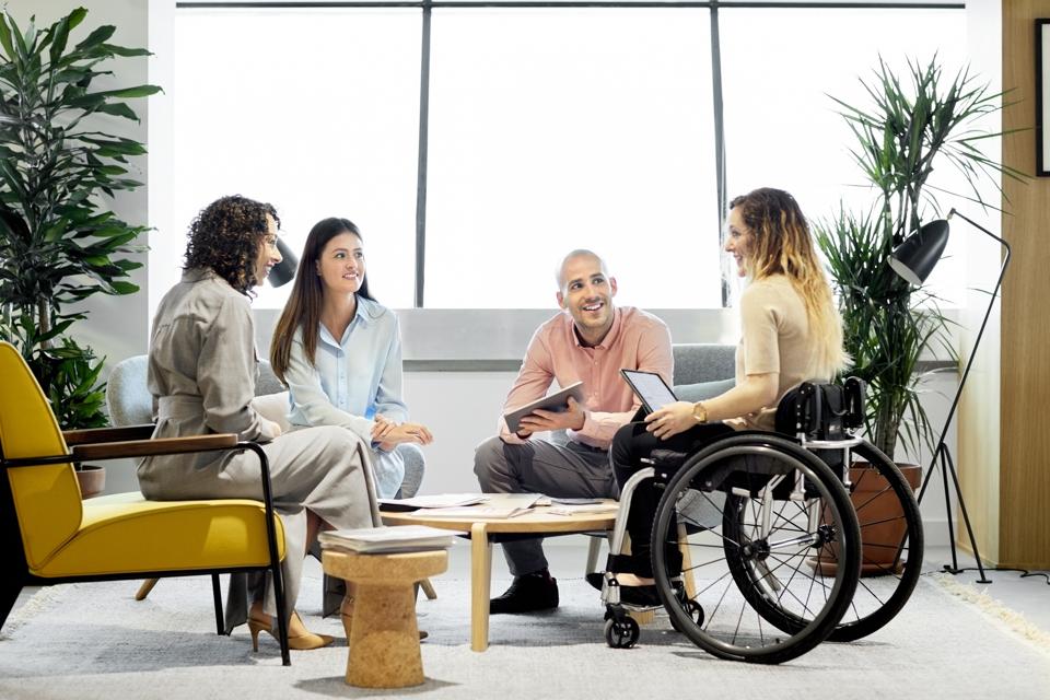 Wheelchair using professional with coworkers in meeting.