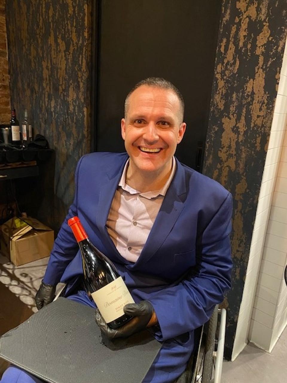 Contento partner a Yannick Benjamin brings a bottle of wine to a table.