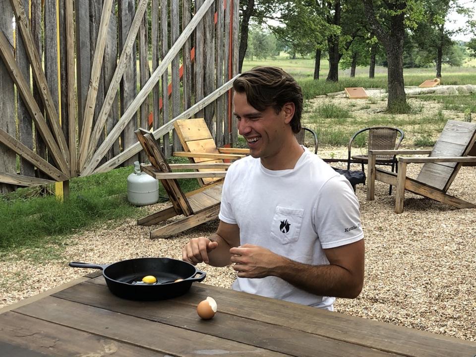 Mares sits at a table outside, cooking an egg with a cast iron skillet