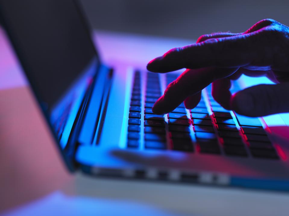Silueta de mano masculina escribiendo en el teclado del portátil por la noche