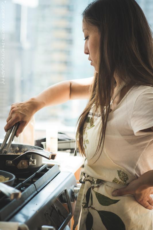 Joanne Molinaro in a white t-shirt with an apron, cooking something in a pan
