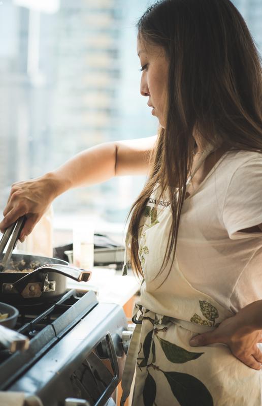 Joanne Molinaro in a white t-shirt with an apron, cooking something in a pan