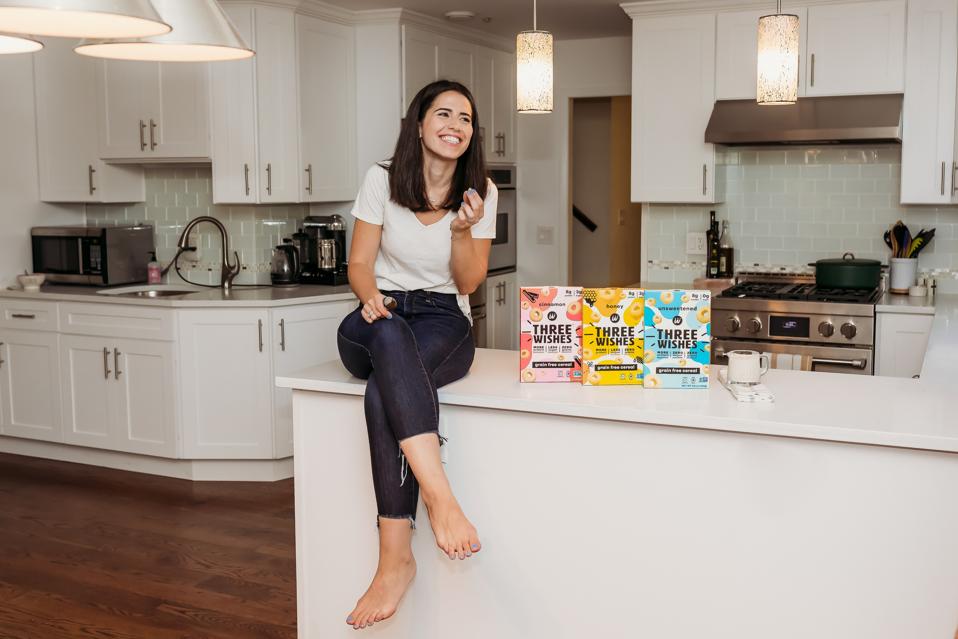 Margaret Wishingrad sits in a kitchen with Three Wishes cereal boxes on counter