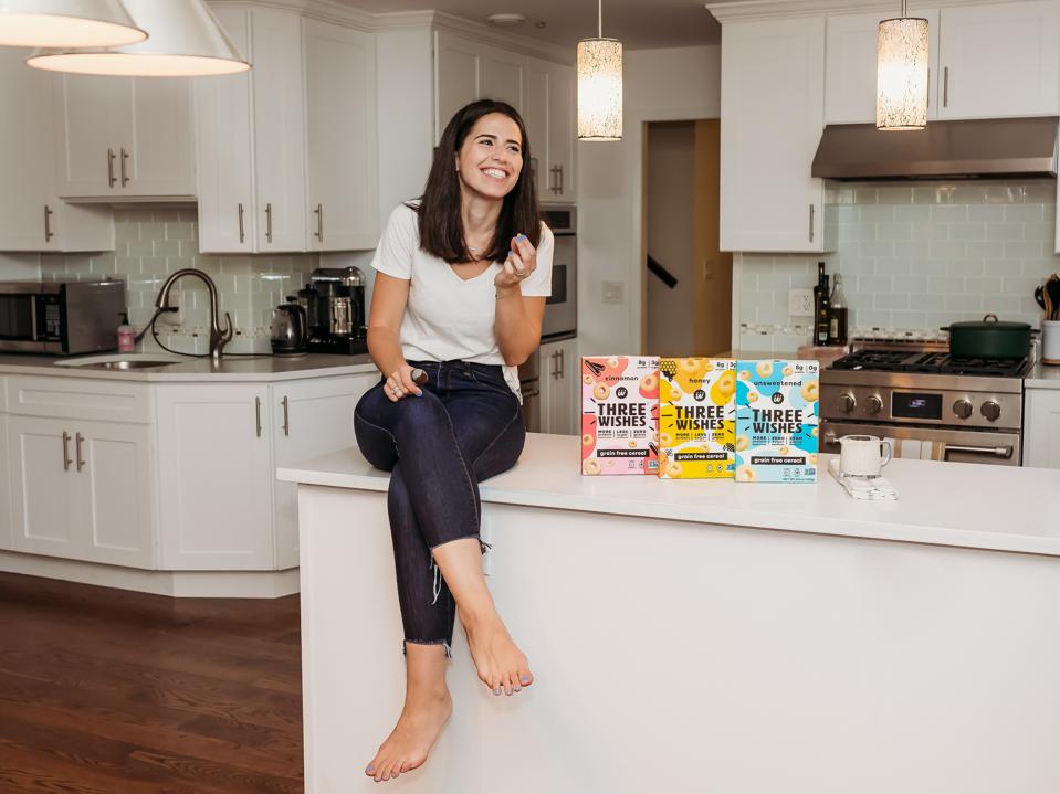 Margaret Wishingrad sits in a kitchen with Three Wishes cereal boxes on counter