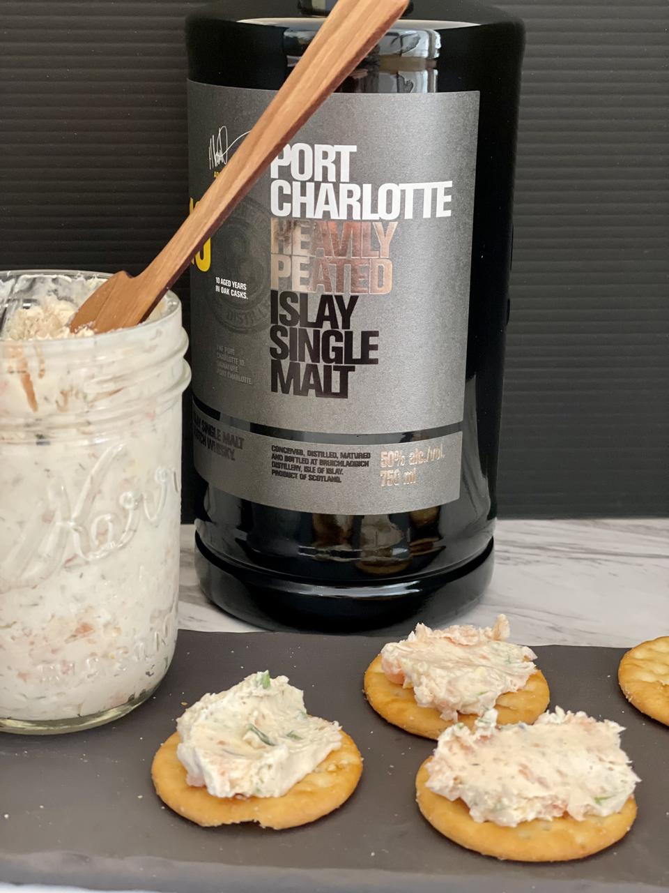 A smoky, peaty Scotch whisky such as Port Charlotte from Bruichladdich is the secret ingredient in The Smoked Salmon Spread, a.k.a. The Spread. The Bottle is shown with a jar of The Spread and three crackers topped with smoked salmon spread.
