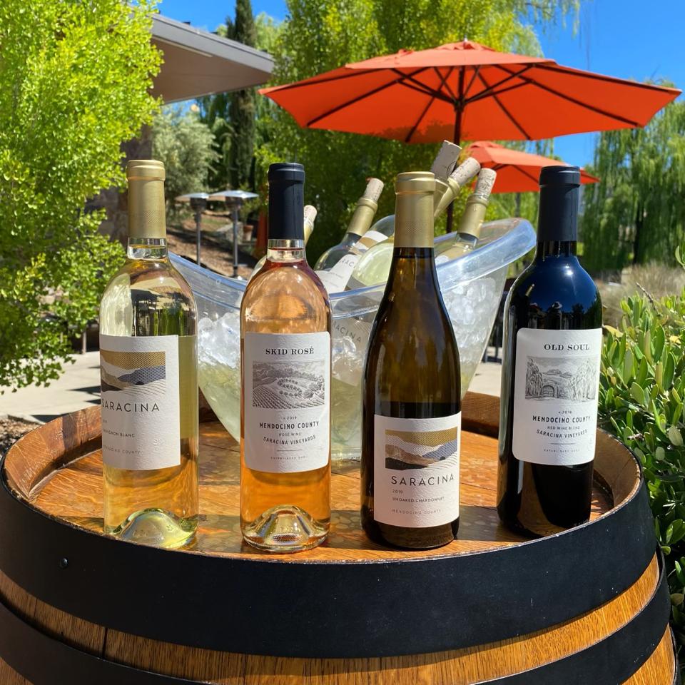 Four bottles of Saracina wine and a bucket of iced wine atop a wine barrel on the patio.