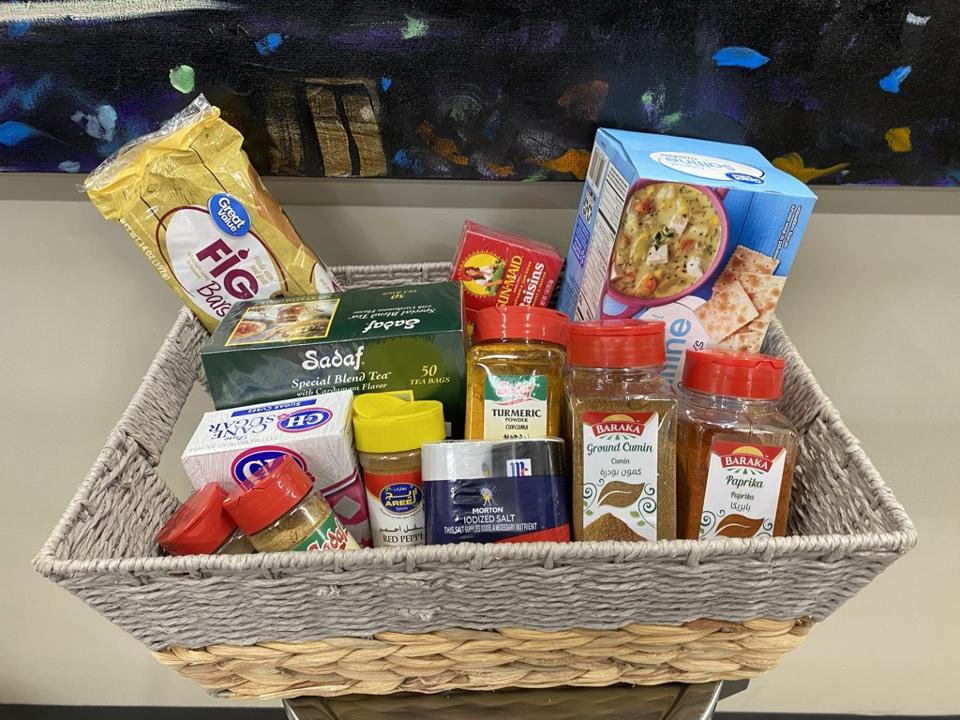 A grey and tan basket full of spices, crackers, tea, sugar, and fig bars