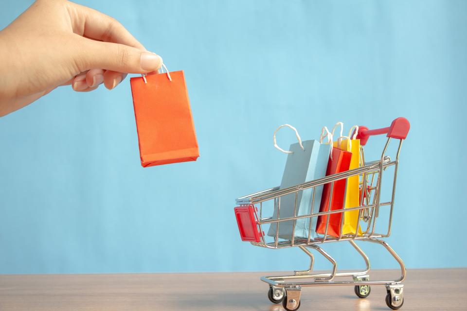Close-Up Of Hand Holding Shopping Bag With Figurine Shopping Cart On Table