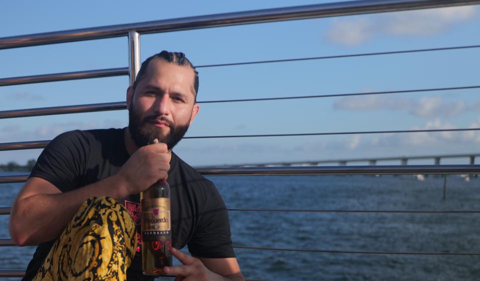 Jorge Masvidal holding a bottle of his mezcal against water background.