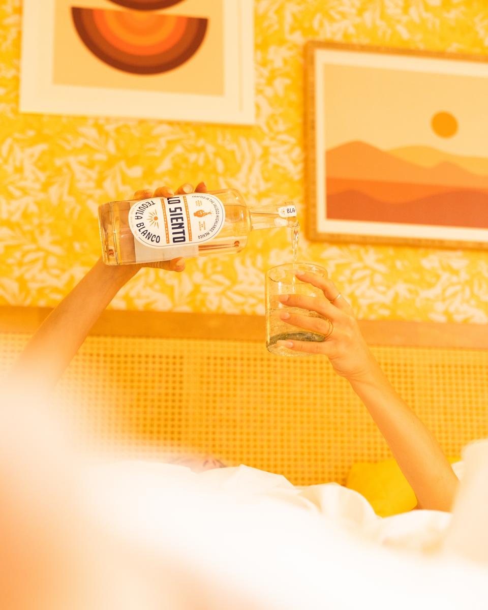 a person is pouring tequila into a glass in a bed.