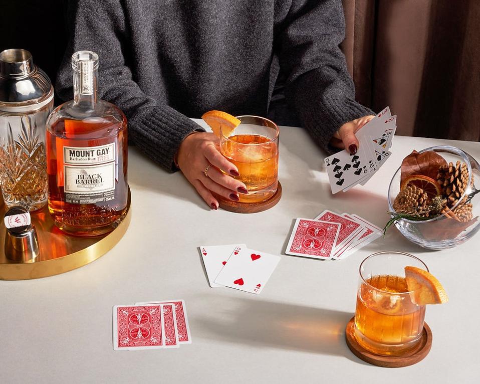 rum on tray with two old fashioned glasses and a woman playing cards with a bowl of pine cones