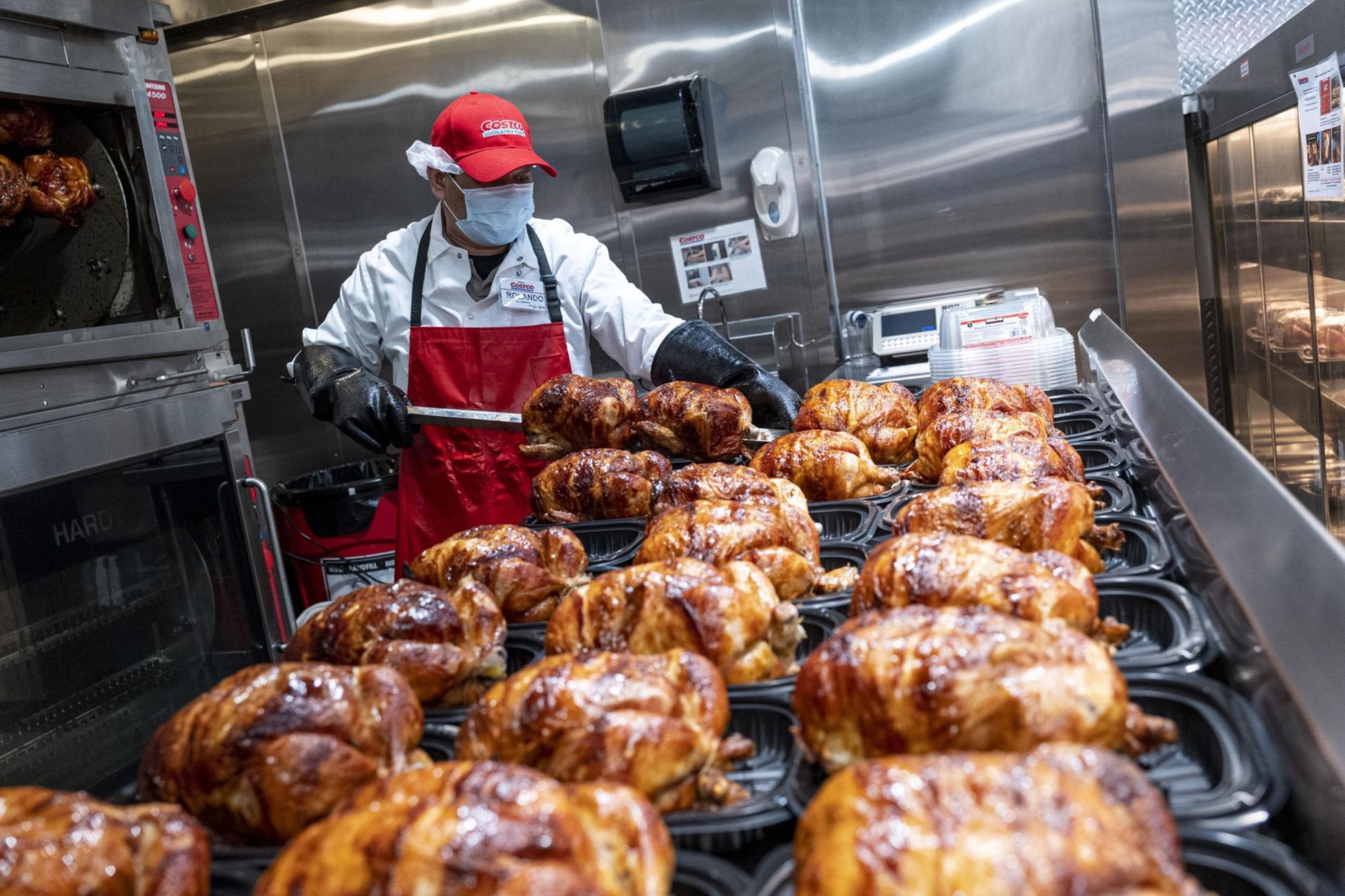 A worker wearing a protective mask removes rotisserie chicken from skewers inside a Costco store in San Francisco, California in March 2021. Photographer: David Paul Morris/Bloomberg