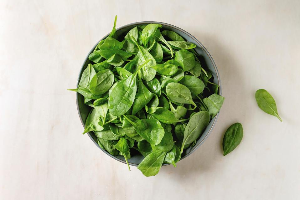 Bowl of fresh Baby spinach leaves over white marble background. Flat lay. copy space