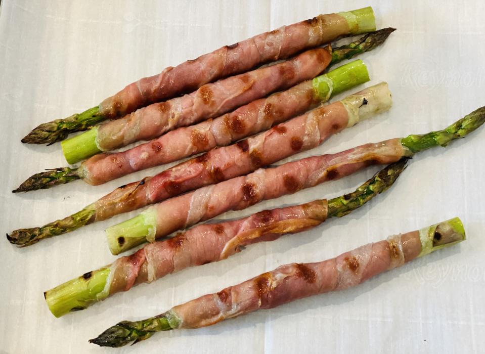 Grilled Prosciutto-Wrapped Asparagus is shown on parchment paper hot off the grill. It makes an unexpected but delicious appetizer or side-dish.