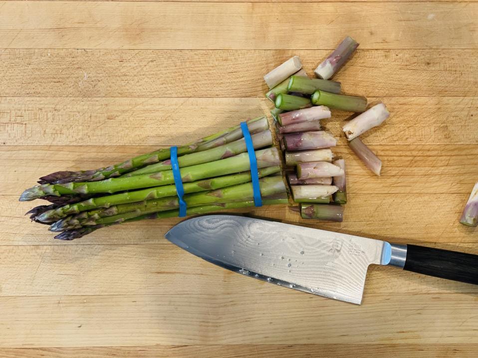 Prep is quick when you use the bottom rubber-band as a guide to cut the woody bottom off the bundle of asparagus. Shown in the photo is a bunch of asparagus and a knife with the tough woody bottoms cut off.