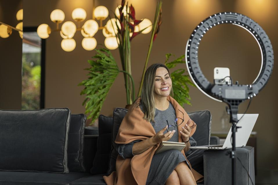 Beautiful woman performing a live from home while using her ring of light to illuminate herself and her cell phone to make the video