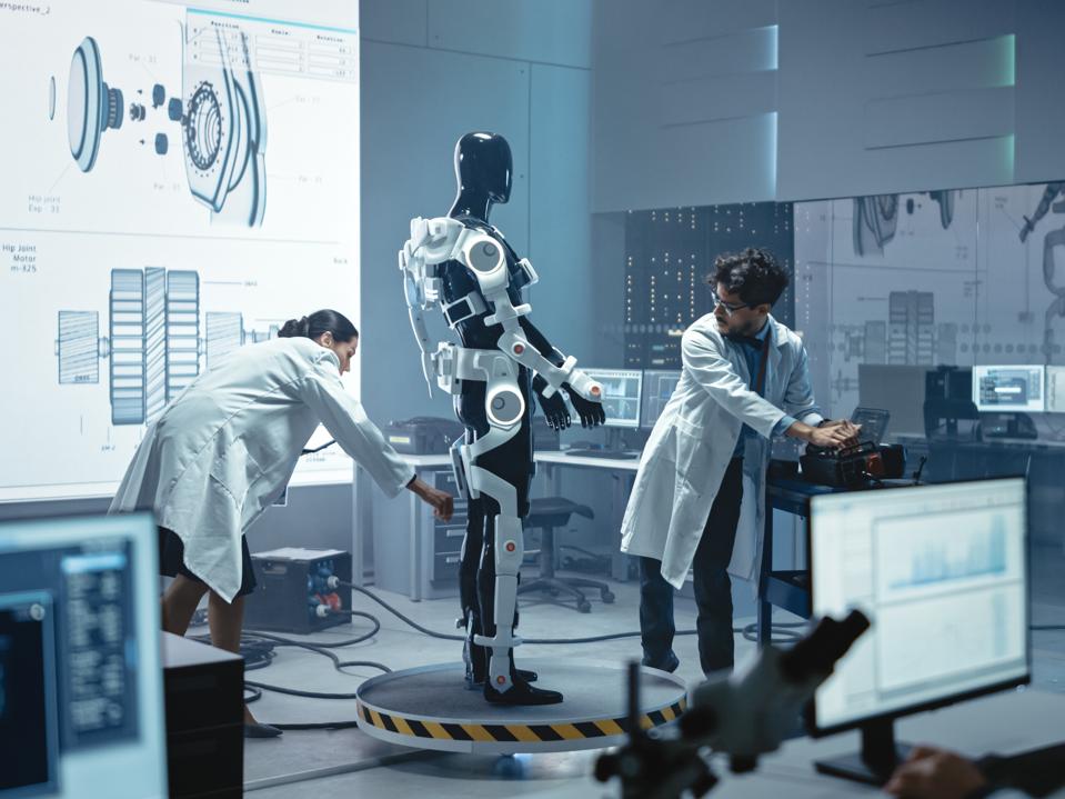 In Robotics Development Laboratory: Chief Female Engineer and Top Male Scientist Work on a Bionics Exoskeleton Prototype. Designing Powered Exosuit to Help Disabled People, Hard Labor Workers