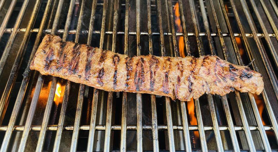 Shown in this photograph is an outside skirt steak on the cooking grate of an outdoor grill set to direct medium-high heat.
