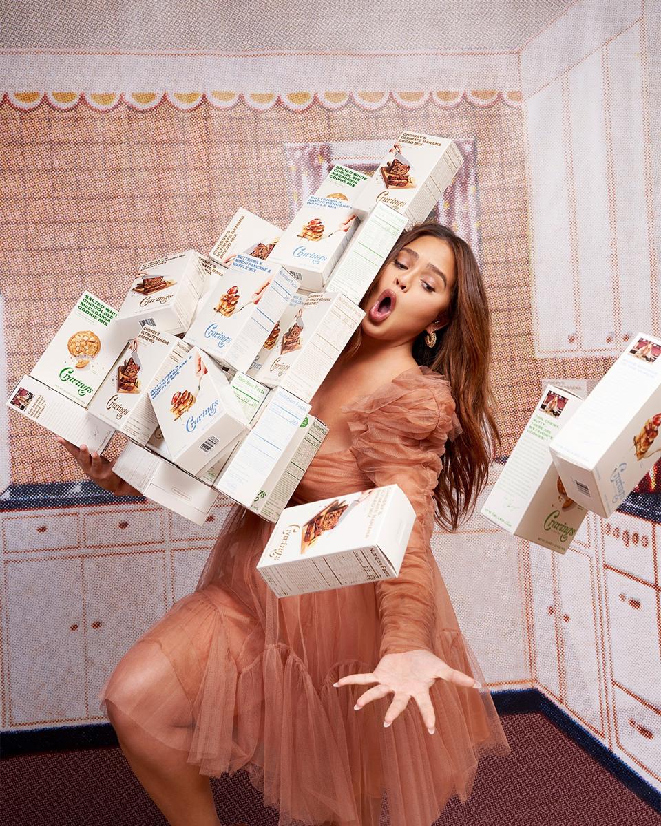 Chrissy Teigen holding several boxes of her new baking mixes.