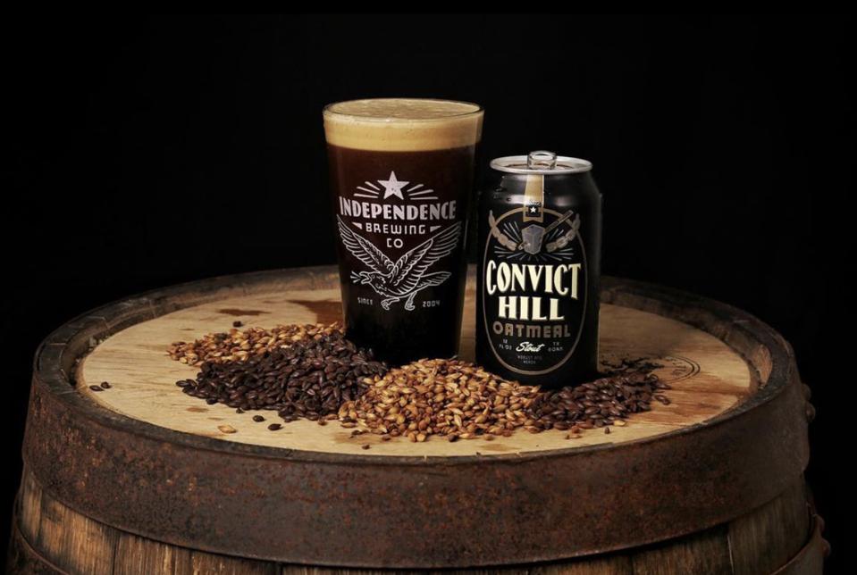Can of Convict Hill Oatmeal Stout and a pint glass full of beer atop a wooden barrel.