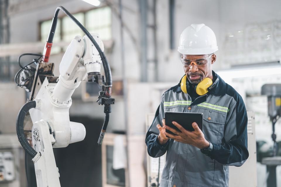 African American engineer working automatic robotic arm machine in factory. Male technician worker maintenance automatic robotic hand in smart factory, industrial and manufacturing concept.