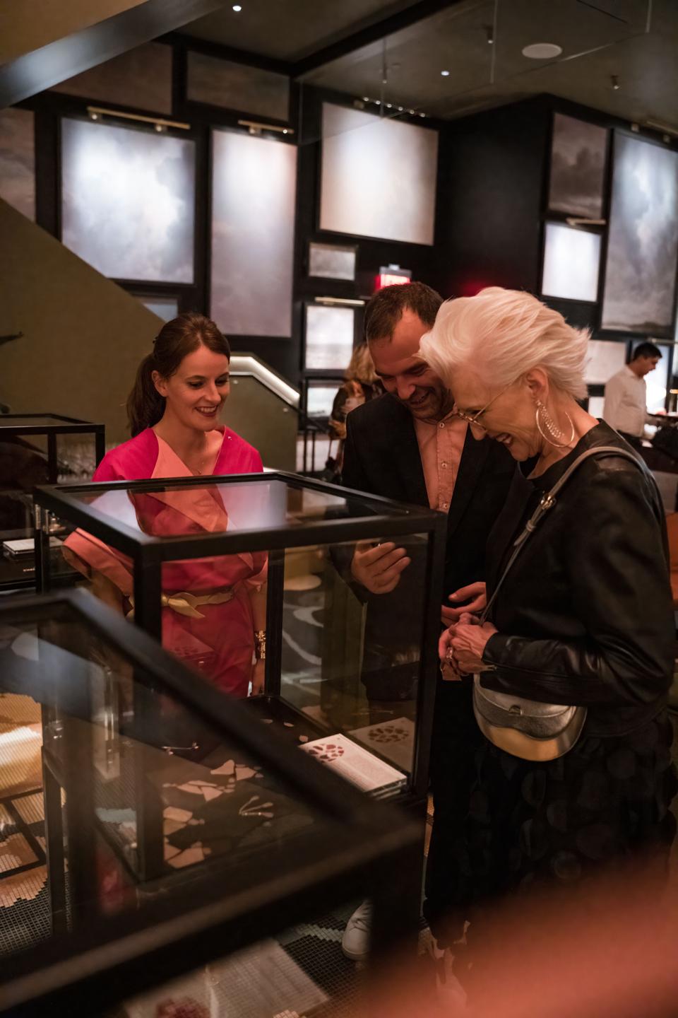 Maud Rabin, director at Rare Champagne, and French artist William Amor, showing Maye Musk his Créations Messagères