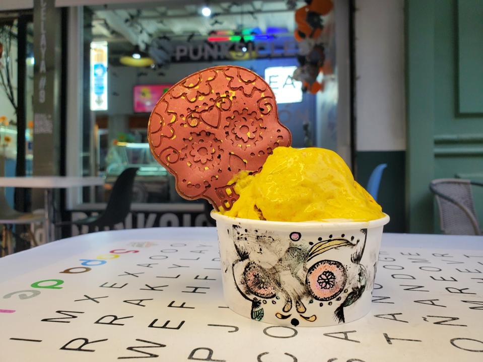 A scoop of ice cream on an outdoor table garnished with a skull-shaped chocolate wafer