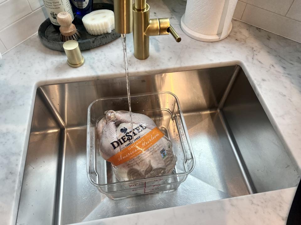 In this photograph by Anthony Underwood, a frozen turkey is shown in a plastic container in a kitchen sink with cold running water turned on so that it will thaw.