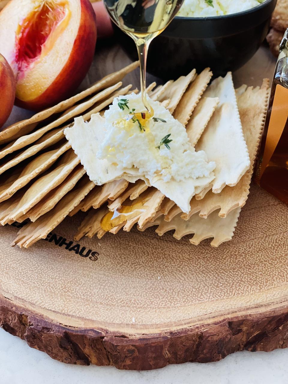 A close-up photograph by Elizabeth Karmel shows fresh Buttermilk Ricotta cheese on a cracker being drizzled with honey.