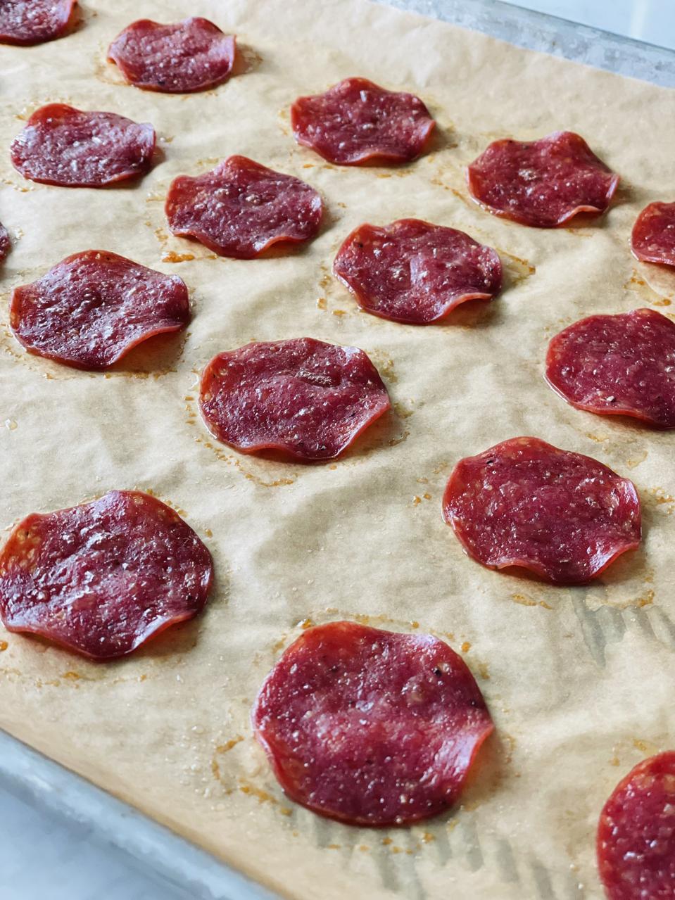 Salami Chips are shown baked on a piece of unbleached parchment paper set into a half-sheet pan in this photograph by Elizabeth Karmel.