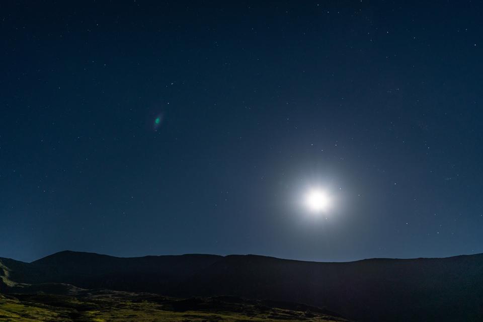 Bright moon and starry night in the mountains over the silhouette of the mountains